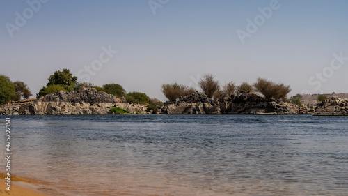 The blue river Nile flows calmly. Ripples on the water. A stretch of sandy beach and picturesque boulders on the opposite shore are visible. Azure sky. Egypt © Вера 