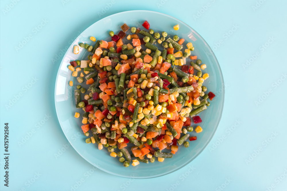 The concept of using quick-frozen products. Frozen vegetables in a light plate on a bright blue background top view.