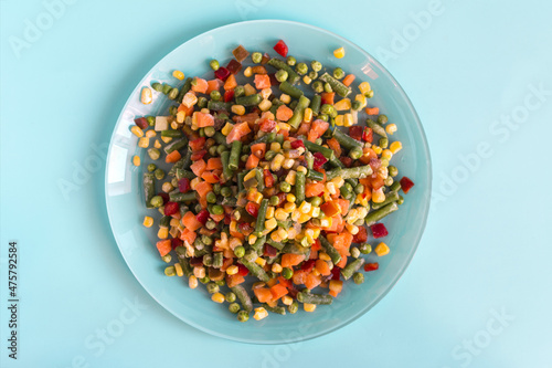 The concept of using quick-frozen products. Frozen vegetables in a light plate on a bright blue background top view.