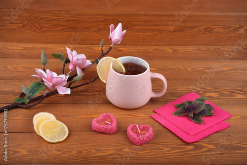 Pink cup of tea with lemon for breakfast.on Valentine s Day. valentine s day.An orchid flower on a branch. Pink napkin. lime leaves. candles in the shape of a heart. Still-life. on a wooden background