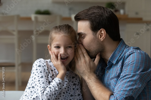 Excited little girl and father sharing secrets or funny news, loving Caucasian dad whispering in adorable 8s girl child ear, family having fun together, talking, enjoying leisure time at home © fizkes