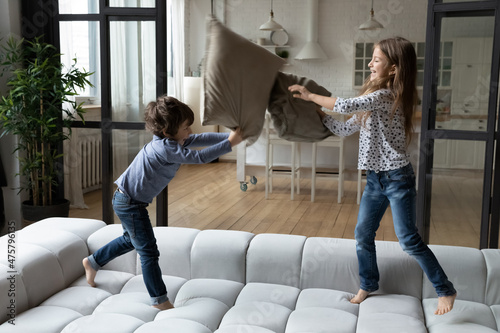 Fotografiet Overjoyed little sister and brother siblings pillow fighting, jumping on cozy co