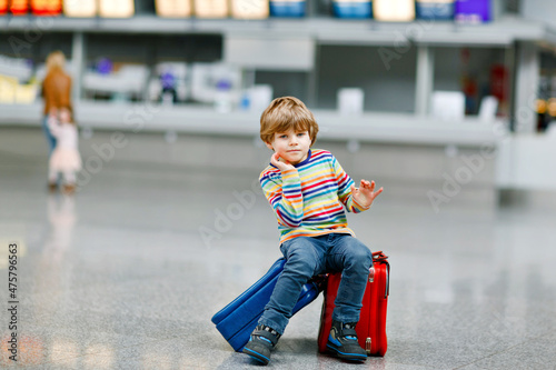 Happy little kid boy with big suitcase luggage at terminal on international airport. Preschool excited child wait for flight and going on vacations. Travel family lifestyle.