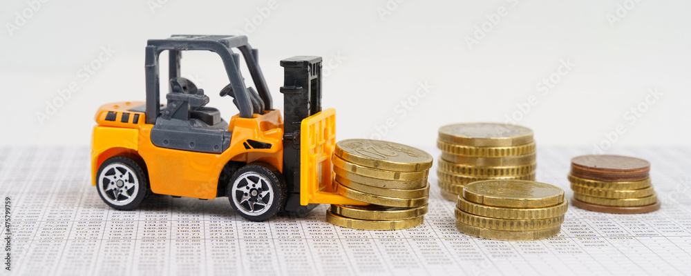 A toy forklift transports coins while driving through accounting documents. A toy forklift transports coins while driving through accounting documents.