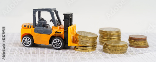 A toy forklift transports coins while driving through accounting documents.