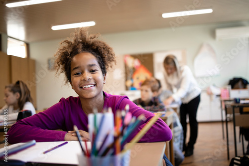 Portrait of smiling Afro American school child sitting in classroom with classmates and children in background.