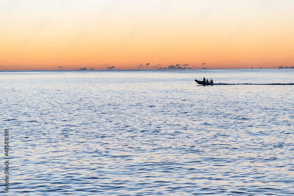 Fototapeta premium Small boat crossing the horizon at sunrise