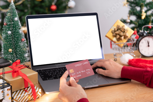 Happy woman holding credit card doing online shopping present at Christmas. Mockup laptop computer with white screen.
