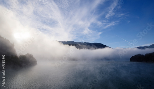 Alpiner Stausee Sylvensteinspeicher im morgendlichen Nebel und Kondensstreifen an einem kalten Tag im Herbst 