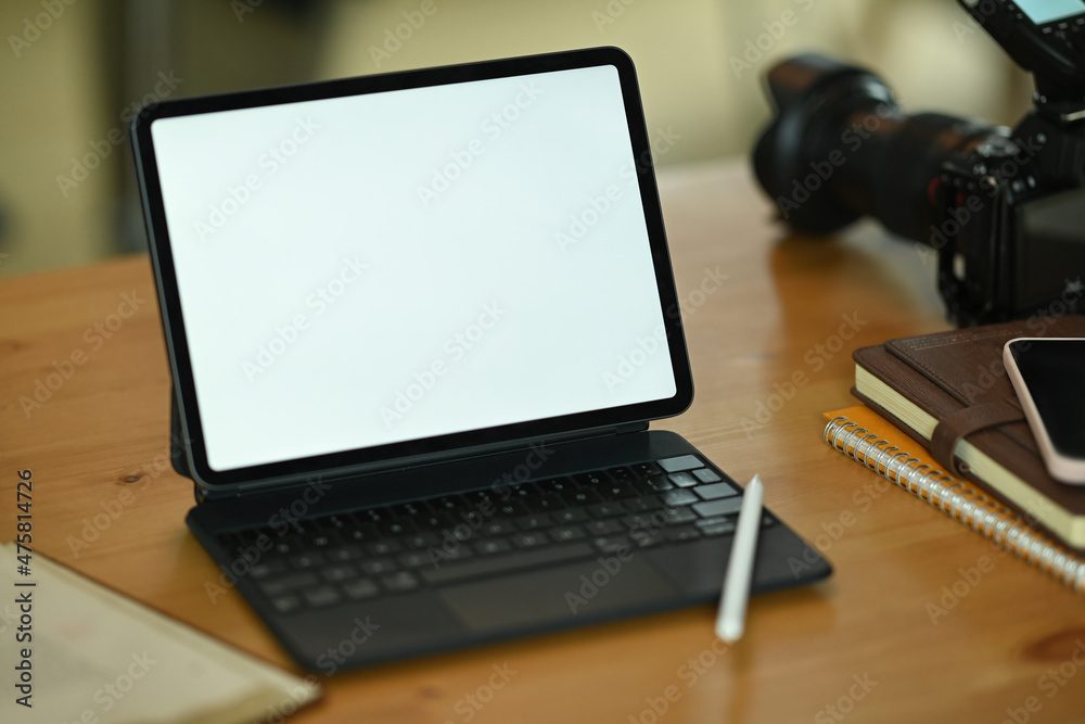 Photo of a white blank screen digital tablet on the wooden table surrounded by a stylus pen, notebook, smartphone, books and digital camera. Photo of a white blank screen digital tablet on the wooden table surrounded by a stylus pen, notebook, smartphone, books and digital camera.