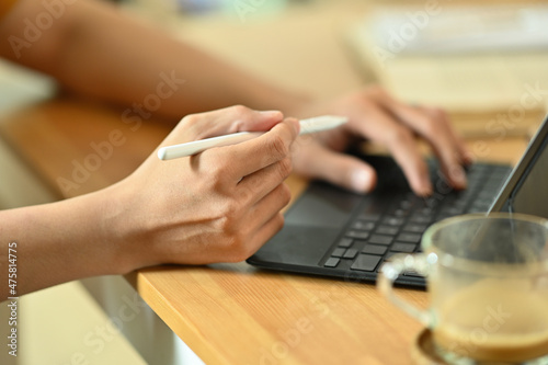 Cropped image of a young freelance man using a digital tablet and stylus pen at the wooden working desk.