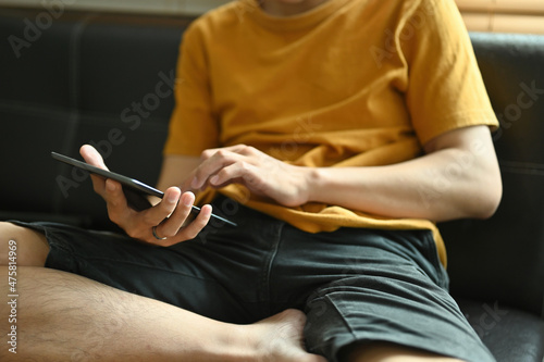 Close-up image of a young man relaxing with a digital tablet on the comfortable sofa.
