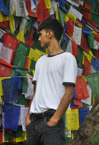 Photos A young man standing outside looking sideways with Buddhist prayer flags in the