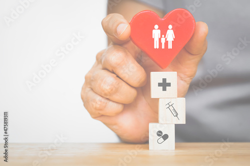 senior's hand holding red heart with family icon on top of health and medical sign on wooden cubes