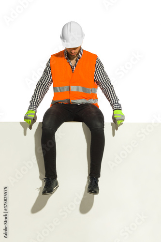 Fotografija Man in white hardhat and reflective waistcoat is sitting on a top of white banner and pointing down