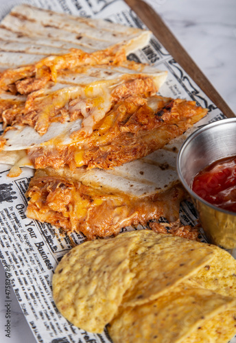 Mexican spicy chicken tinga quesadillas served with lime wedges, salsa, and nachos.