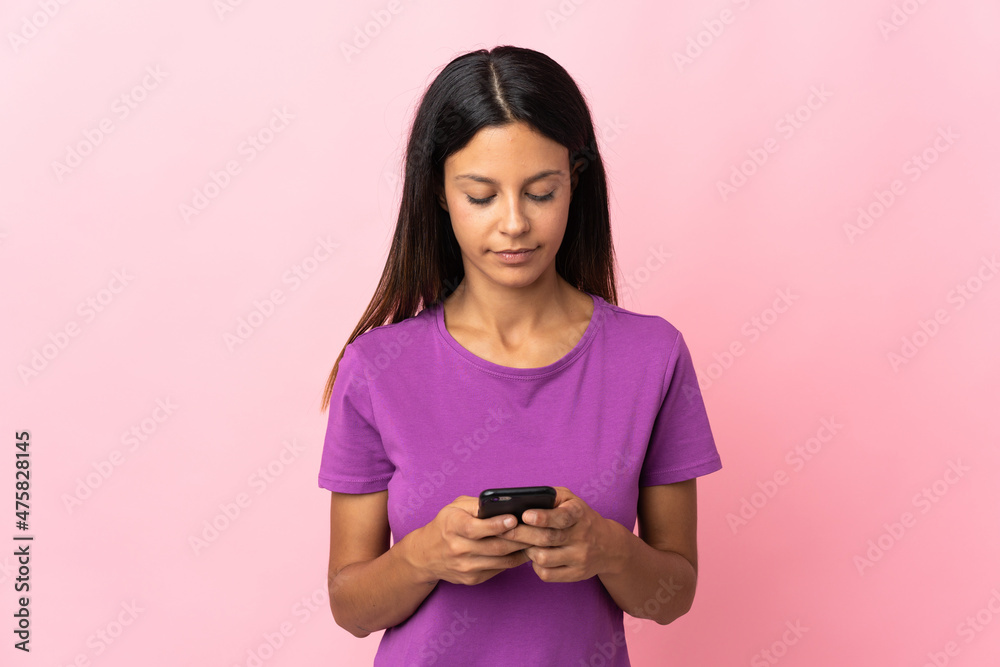 Caucasian girl isolated on pink background using mobile phone