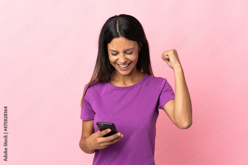 Caucasian girl isolated on pink background using mobile phone and doing victory gesture Caucasian girl isolated on pink background using mobile phone and doing victory gesture