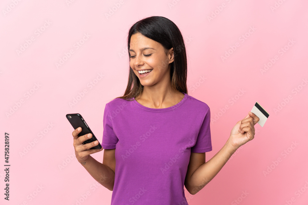 Caucasian girl isolated on pink background buying with the mobile with a credit card Caucasian girl isolated on pink background buying with the mobile with a credit card