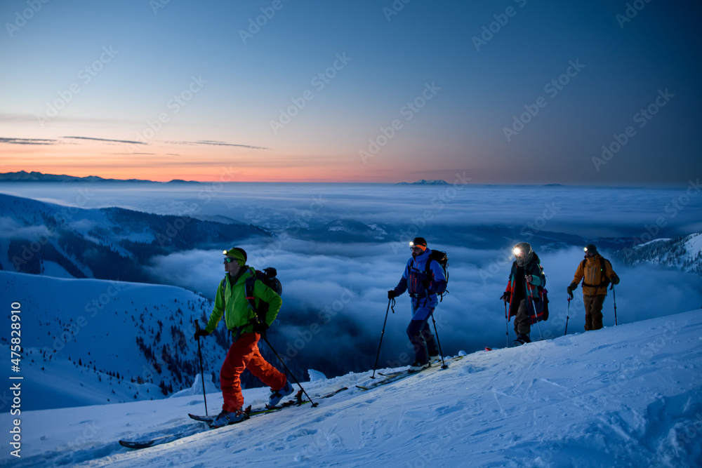 group of skiers with flashlights walking along mountain slope against the backdrop of picturesque evening sky