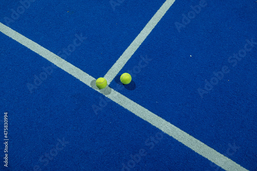 Two paddle tennis balls in the foreground on the line of a blue paddle tennis court at night. © Vic