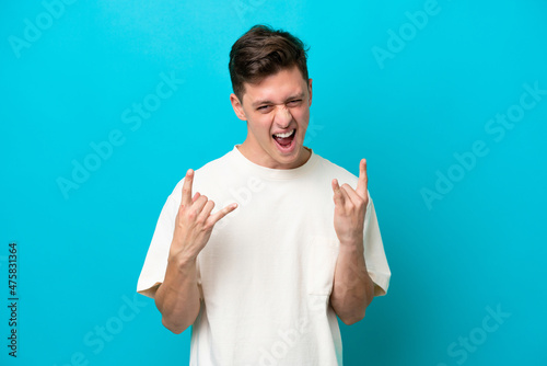 Young handsome Brazilian man isolated on blue background making horn gesture