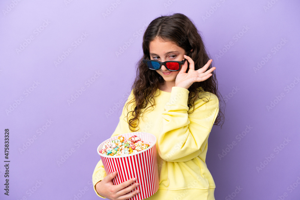 Little caucasian girl isolated on purple background with 3d glasses and holding a big bucket of popcorns Little caucasian girl isolated on purple background with 3d glasses and holding a big bucket of popcorns