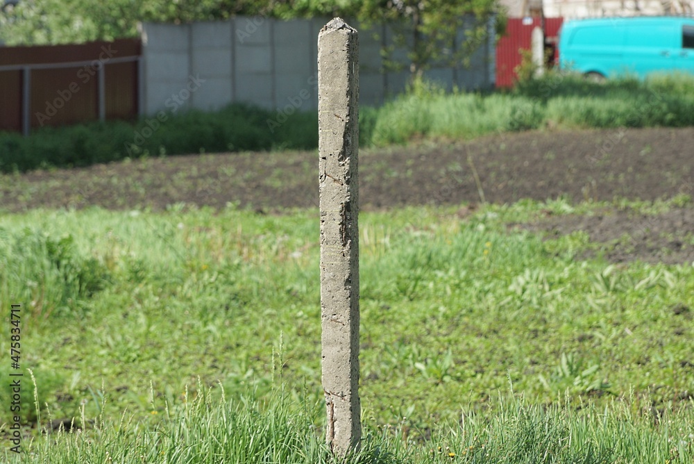 one old gray long concrete pillar stands on the street in green grass