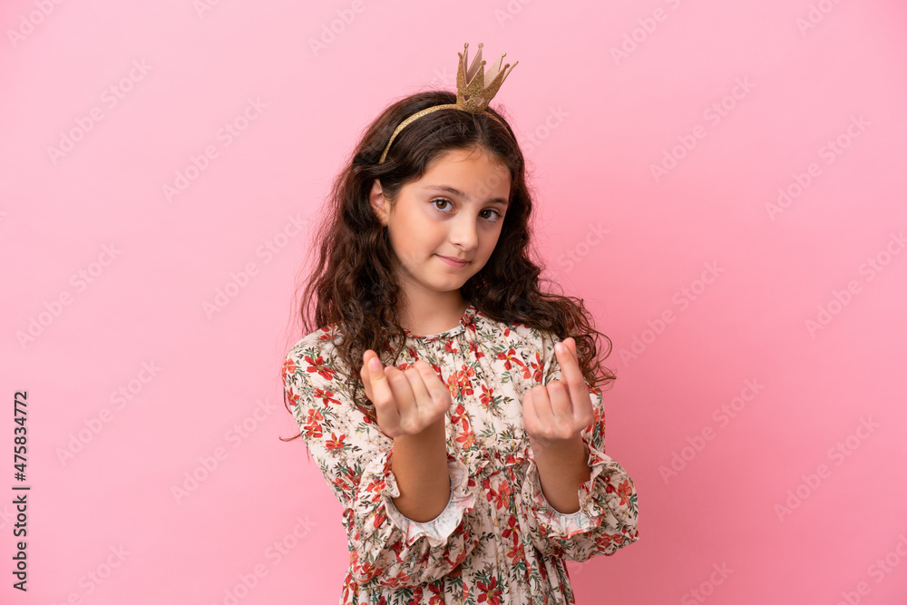 Little caucasian princess with crown isolated on pink background making money gesture