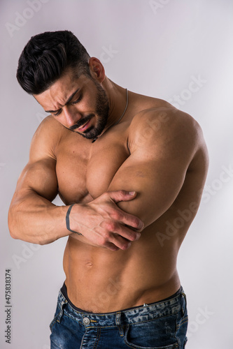 Muscular man holding his elbow with one hand and grimacing in pain