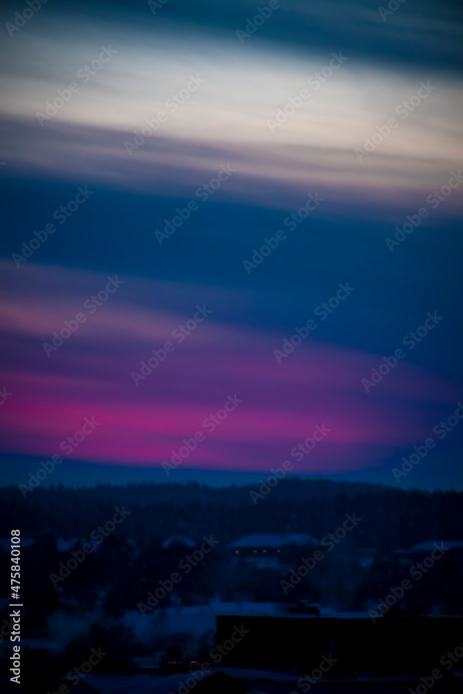 Blurred colorful sunset sky in Lithuania. Bright pink clouds illuminated by setting sun, dark forest in winter. No selective focus, defocused background.