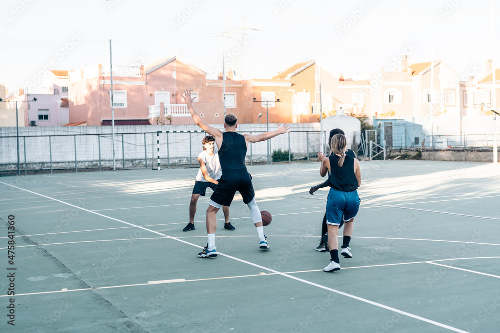 Fototapeta premium Four friends playing basketball together in an outdoors court