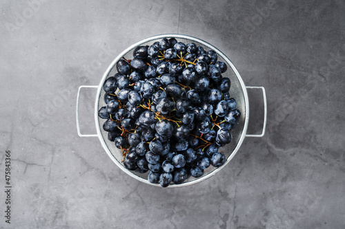 Sweet black grapes in a metal bowl on a dark textured background.