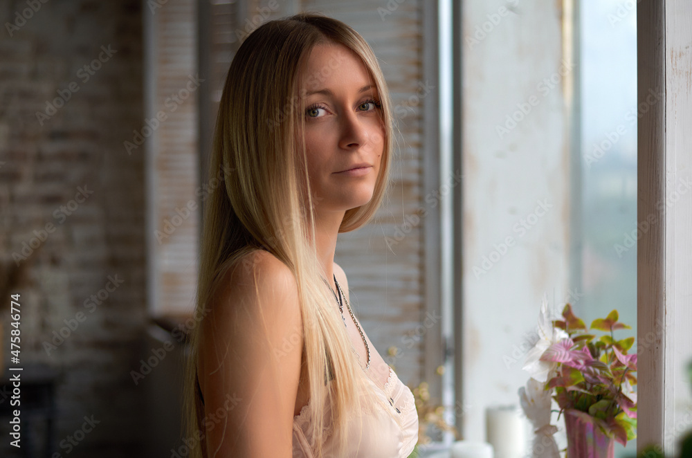 portrait of a beautiful blonde girl near the window.looks at the camera. portrait of a beautiful blonde girl near the window.looks at the camera.