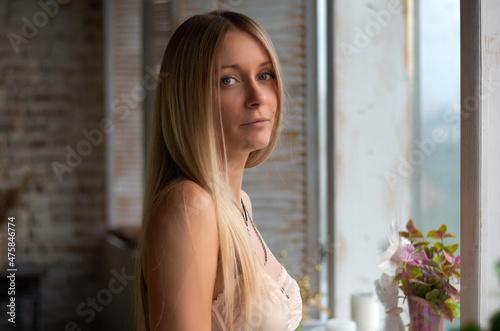 portrait of a beautiful blonde girl near the window.looks at the camera.