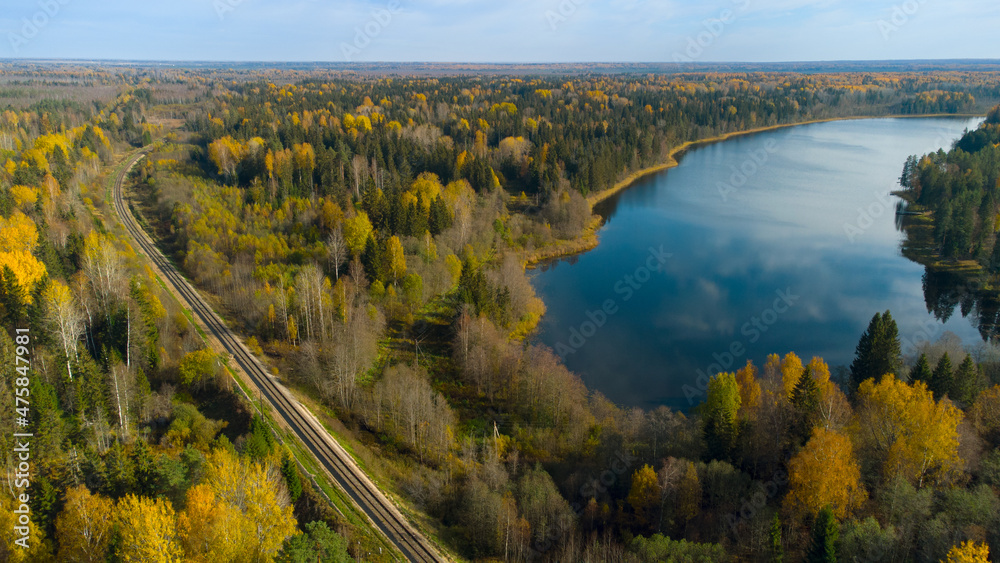 A beautiful view from above of the autumn forest and lake, the view from the drone. The railway passes through the forest. A beautiful view from above of the autumn forest and lake, the view from the drone. The railway passes through the forest.