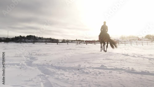 Woman riding her horse one cold winter day. Sun beams in the snow. Northern winter sun light. 4K drone footage, slow motion x2.