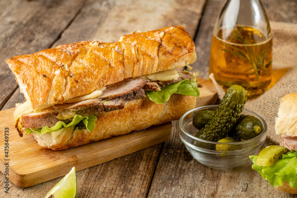 Sandwich with meat, vegetables and cheese on a wooden table.