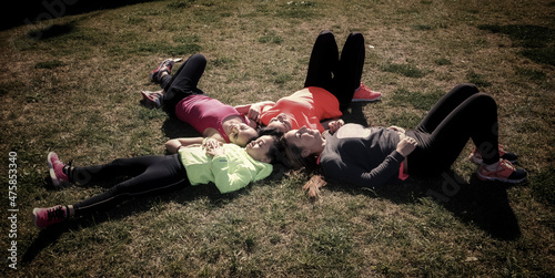 Fotografía cenital de cuatro mujeres de distintas edades tumbadas boca arriba en la hierva disfrutando del sol de la primavera. photo