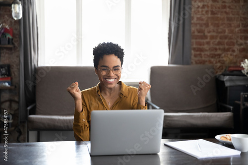 Tela Happy laughing young African American woman in glasses looking at computer screen, clenching fists making yes gesture, celebrating getting dream job offer or amazing win news, internet success