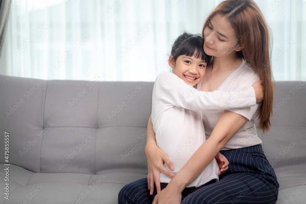 people and family concept - happy smiling girl with mother hugging on sofa at home