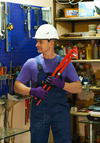 a white man in overalls with a red tool in his hands in the workshop. The locksmith is getting ready for work