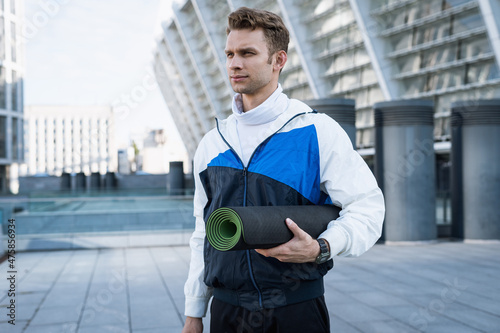 Sportive man standing outdoors with yoga mat