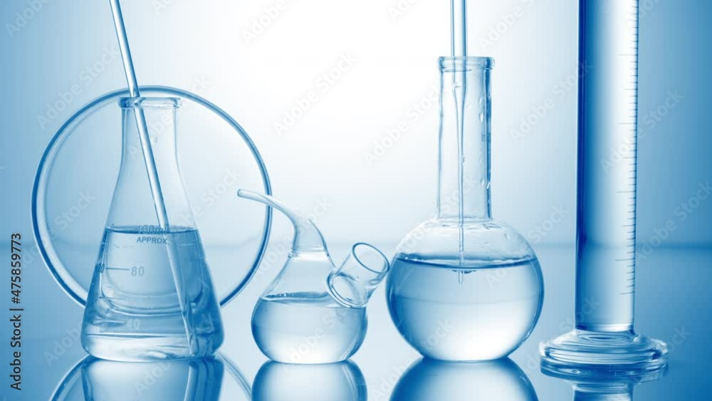 Long dropper is lowered into clear flask with water surrounded by lab glassware on pale blue background | Abstract skin care cosmetics formulation concept