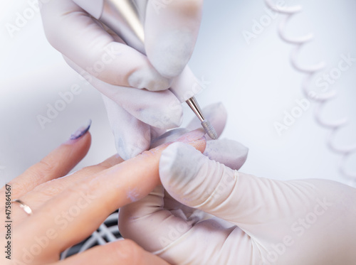 close-up photo of nail treatment with an electric file. The manicurist removes gel polish from the nail with a nail drill.