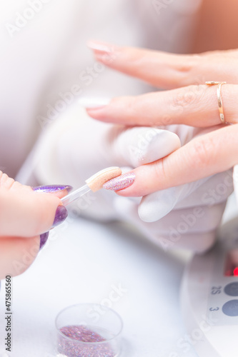 applying bright glitter on a customer's nails in a beauty studio
