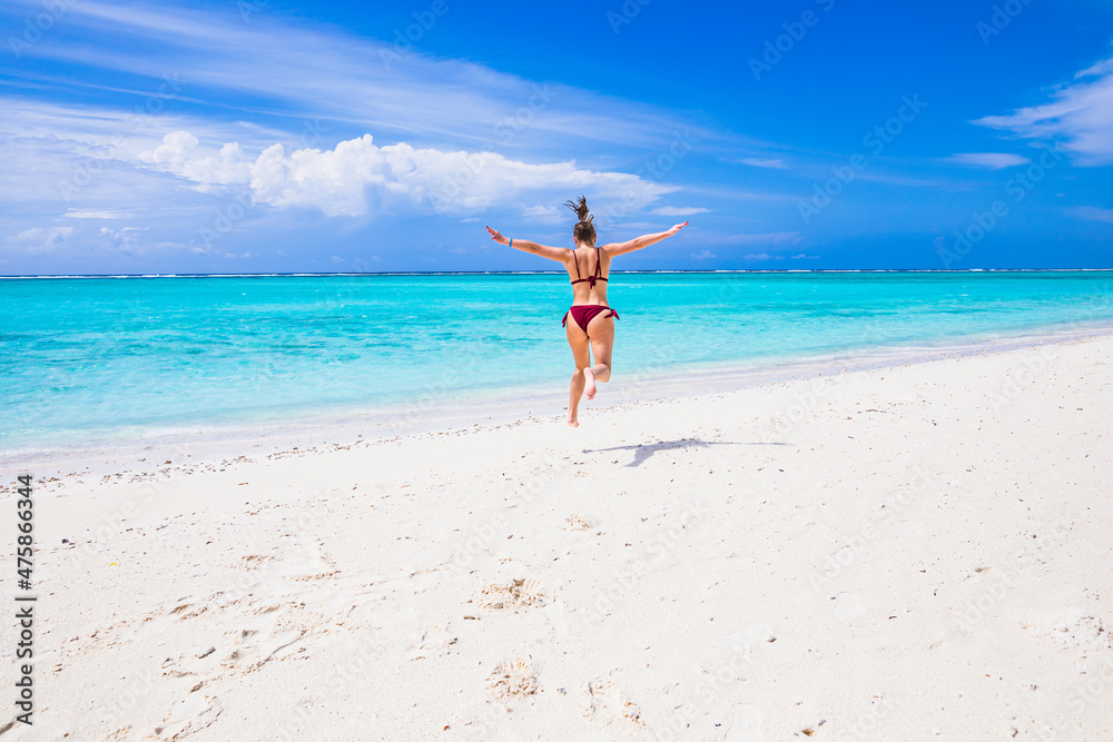 A cheerful girl jumps up on a paradise beach in the Maldives