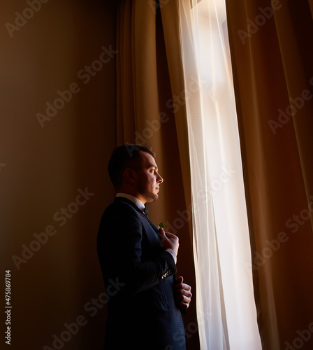 young man in a white shirt fastens cufflinks on sleeves near the window. business portrait. The groom is going to meet the bride. Wedding.