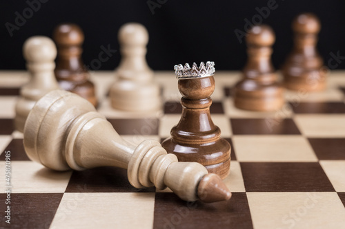 A black chess pawn with a crown on the chessboard, a defeated white chess king lies next to it. The concept of success and self-belief. Motivation.
