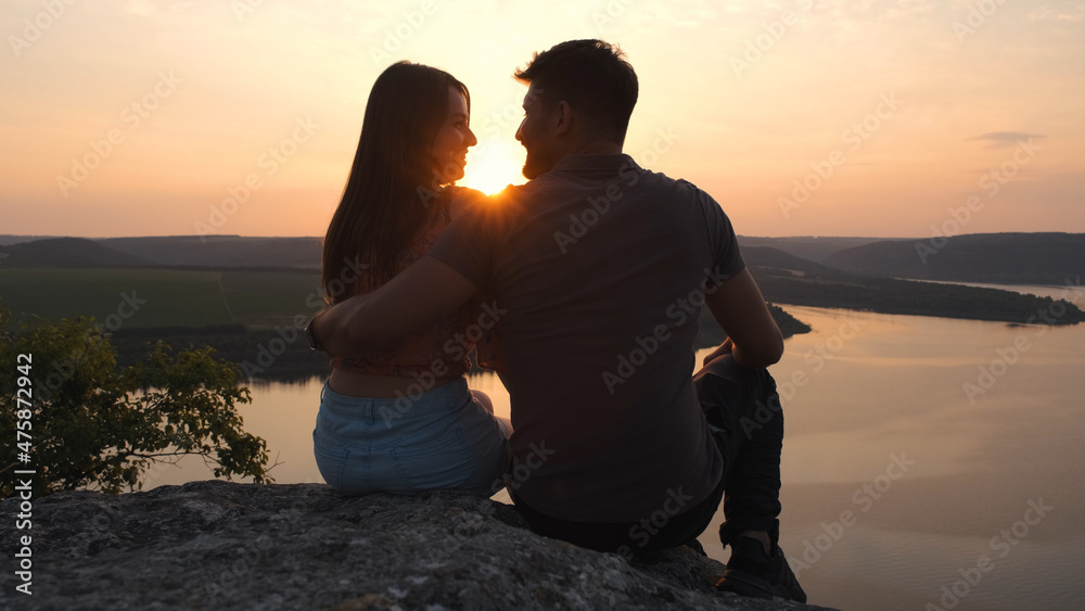The young couple sitting on rocky mountain above the beautiful river